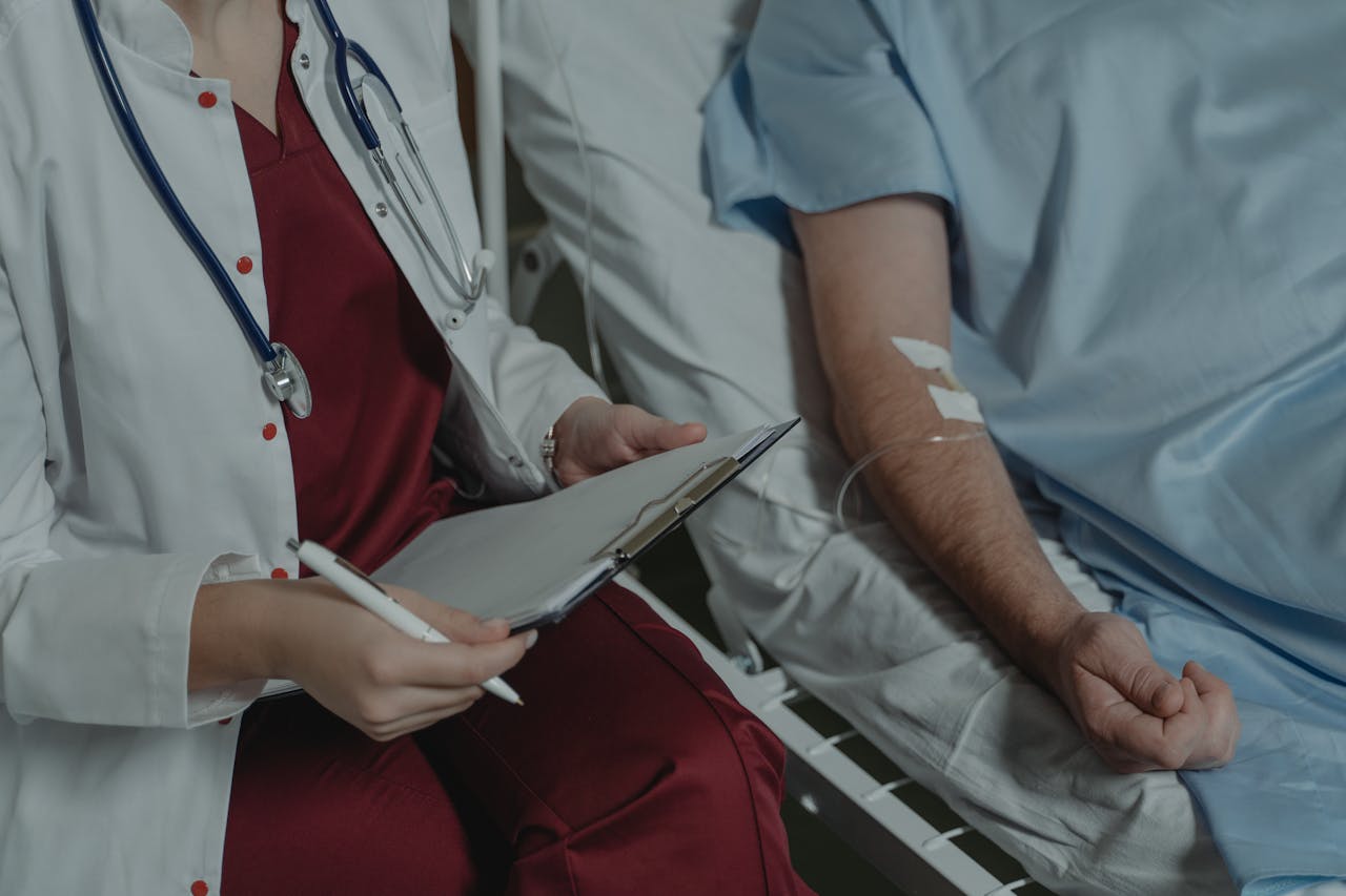 Doctor reviewing medical chart while assisting a patient in a hospital bed.